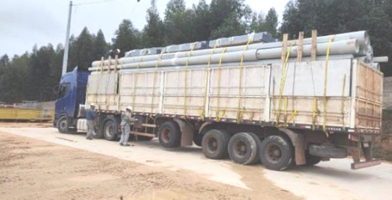 Carreta da LI ENERGIA carregada com postes de concreto e materiais elétricos, pronta para deslocamento